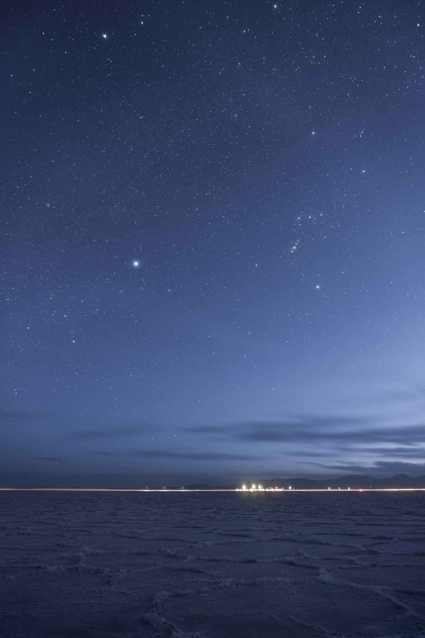 Blueish sky with stars, Orion prominant, salt flats, rest stop lights in the distance